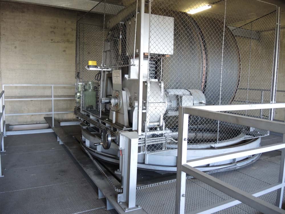 Großes mechanisches Gerät in Schutzkäfig auf Plattform mit Industrieboden und Betonwänden