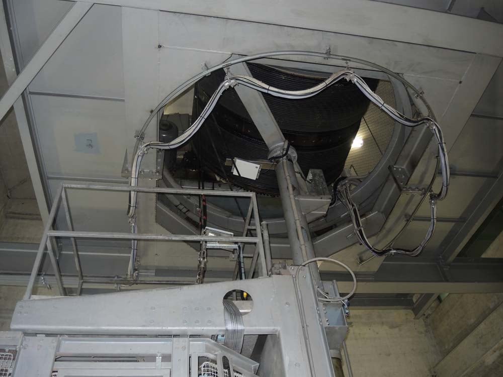 Blick auf Industriemaschinen mit Metallstrukturen, Kabeln und einem runden Bauteil in einer Betonanlage