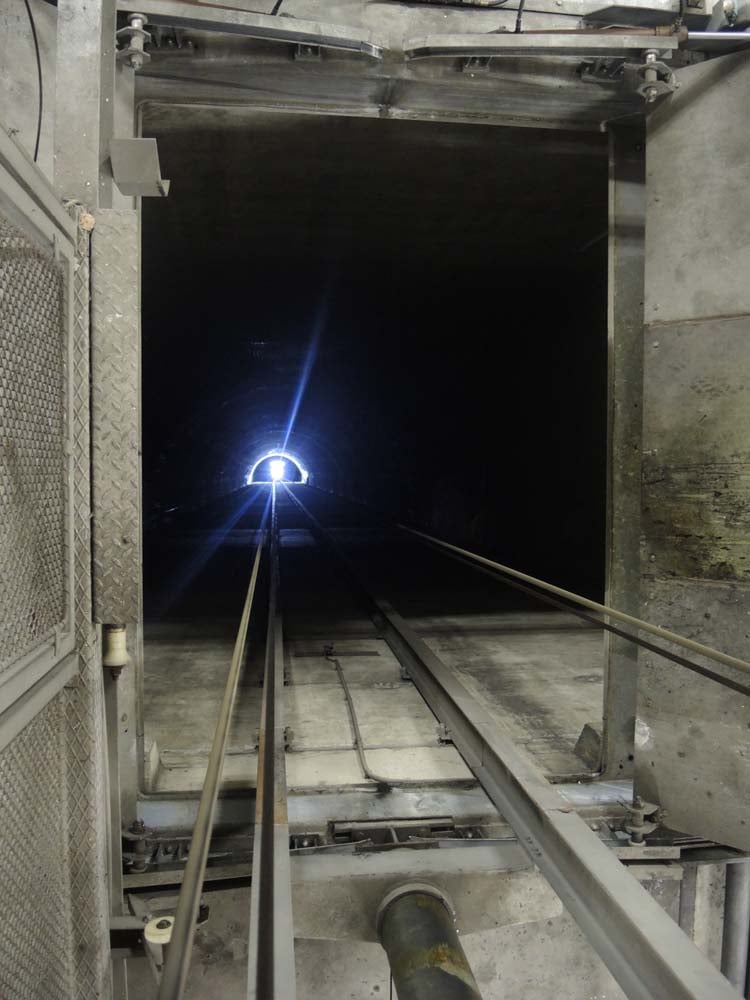 Dunkler Tunnel mit Gleisen, die zu einem hellem Licht am Ende führen, umgeben von Industriewänden