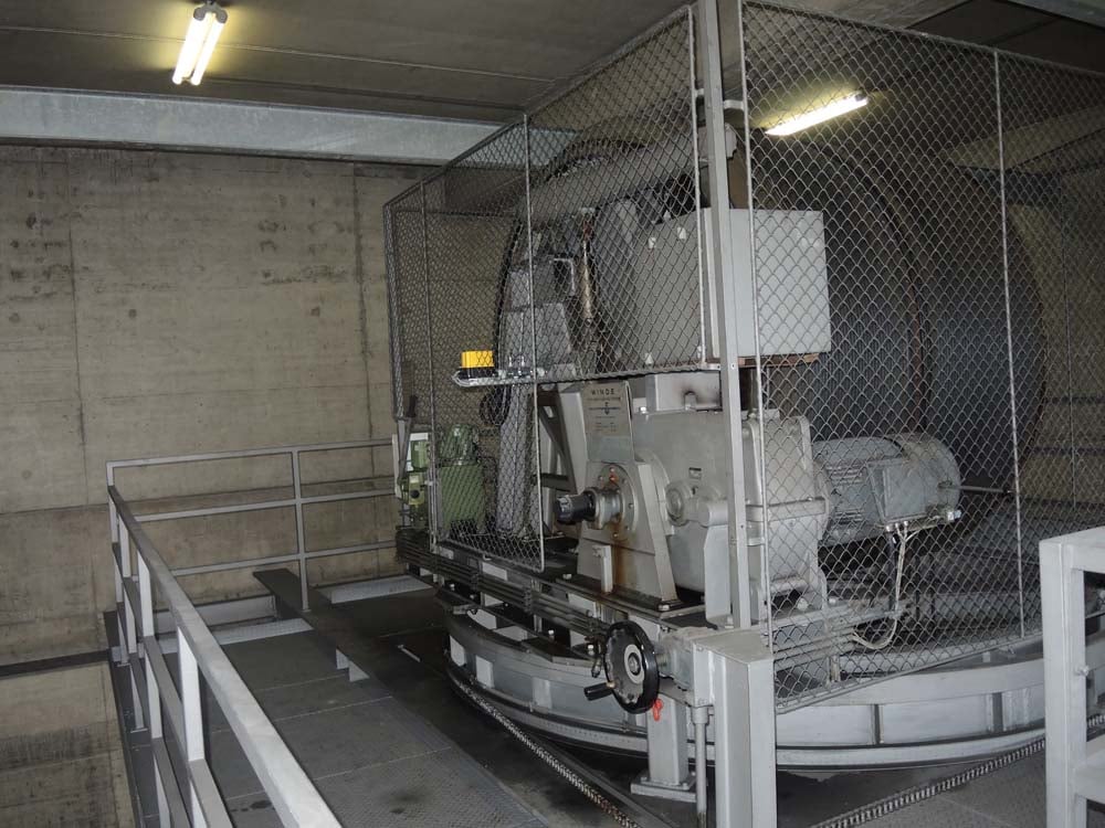 Großes mechanisches Gerät in Schutzkäfig auf Plattform mit Industrieboden und Betonwänden