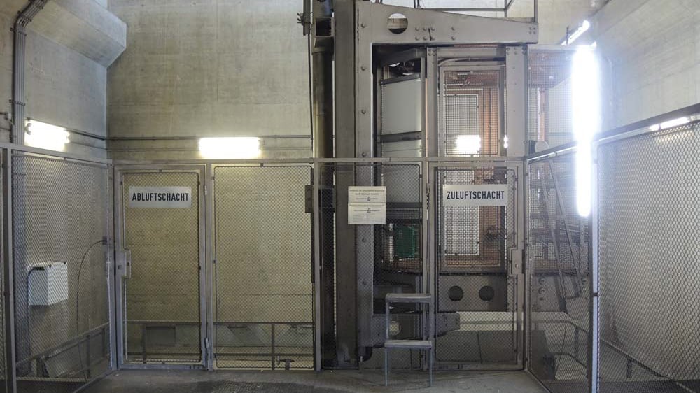 Industrieanlage mit Metallgittern und Beschilderung für Abluft- und Zuluftschächte in einem technischen Gebäude mit Betonwänden