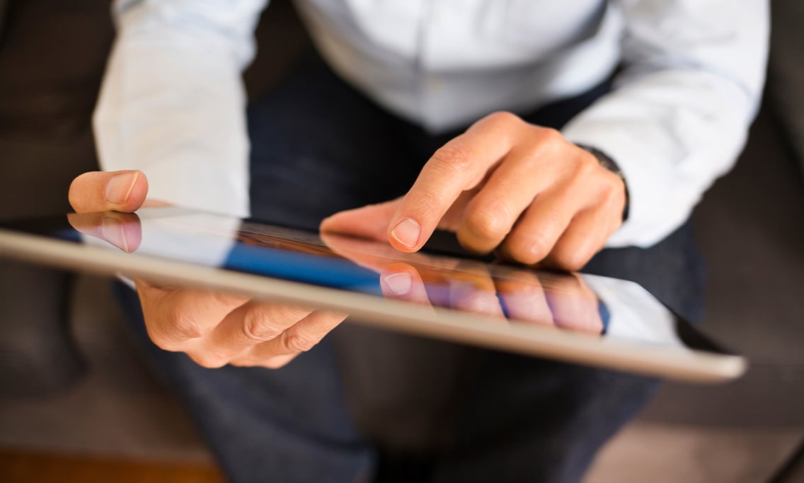 Eine Person in einem weißen Hemd interagiert mit einem Tablet und tippt sitzend auf dessen Bildschirm.