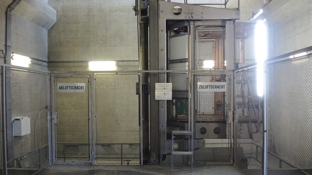 Industrieanlage mit Metallgittern und Beschilderung für Abluft- und Zuluftschächte in einem technischen Gebäude mit Betonwänden